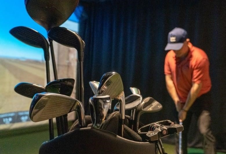 A man golfing on a simulator with clubs in the foreground.