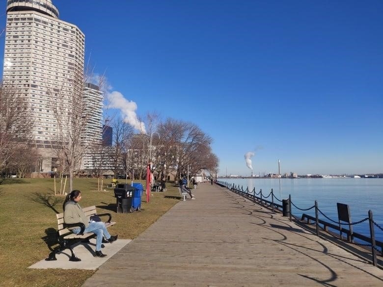 A woman in a winter jacket sits on a bench along Toronto’s harbourfront.  