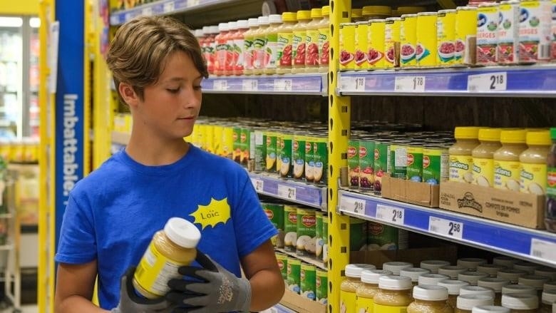 A young boy, 13, working in a grocery store. He's holding a can of apple sauce.