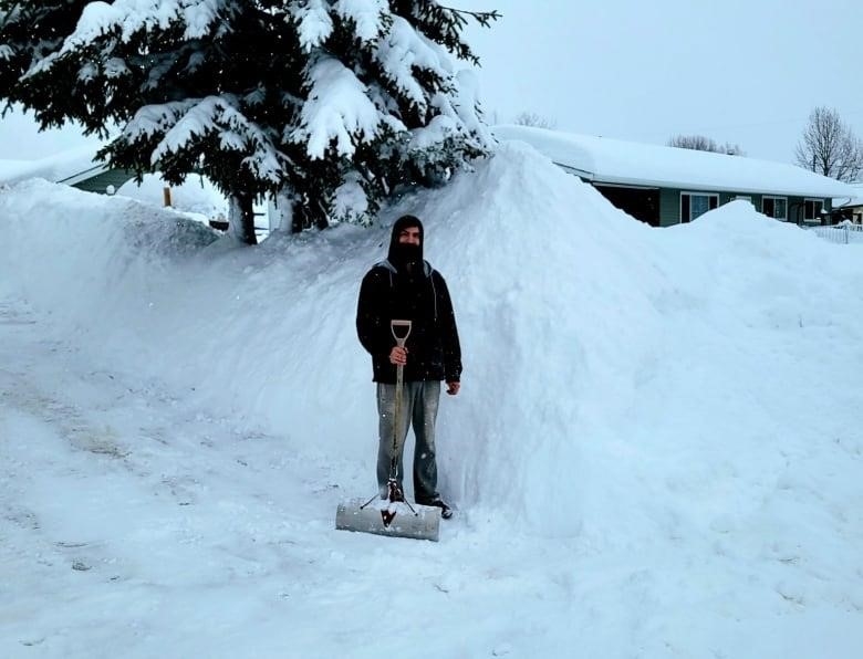 A man with a shovel stands in front of a snowbank.