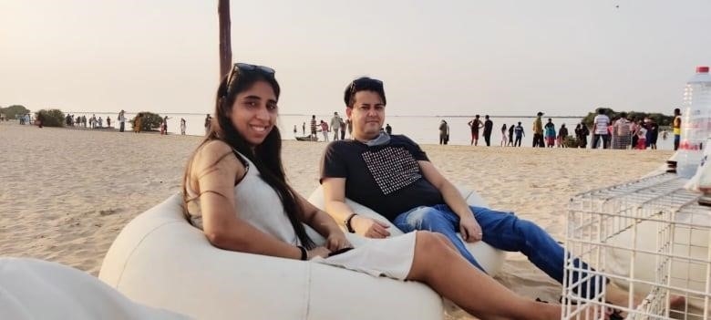 A smiling woman and man sit on inflatable chairs on a sandy beach.