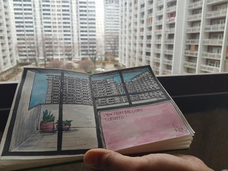 A hand holds up a sketchbook with a drawing of the same view from a balcony overlooking a courtyard in the background.