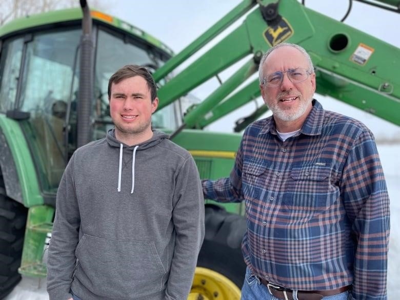 Maxwell Olson (left) and father Mark Olson pose on their family farm in front of a green tractor.