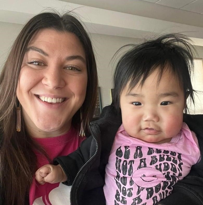 A woman holding an infant smiles at the camera.