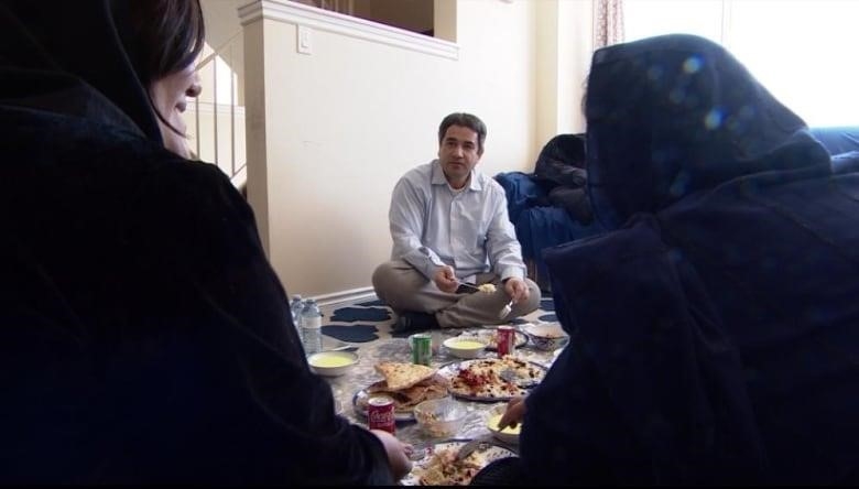 A man sits on floor with his family to eat Nowruz festive food.