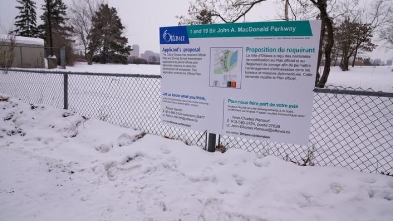 A development sign is attached to a chain-link fence in the snow.