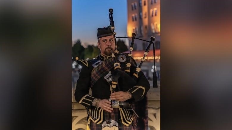 A man wearing dark traditional bagpipe clothing plays the bagpipes with the Chateau Laurier in the background. Close up shot of the bagpiper.