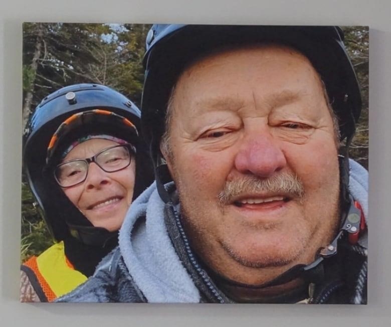 A man and a woman smile at the camera. They're wearing helmets and the woman is wearing an orange safety vest and an orange hat. 