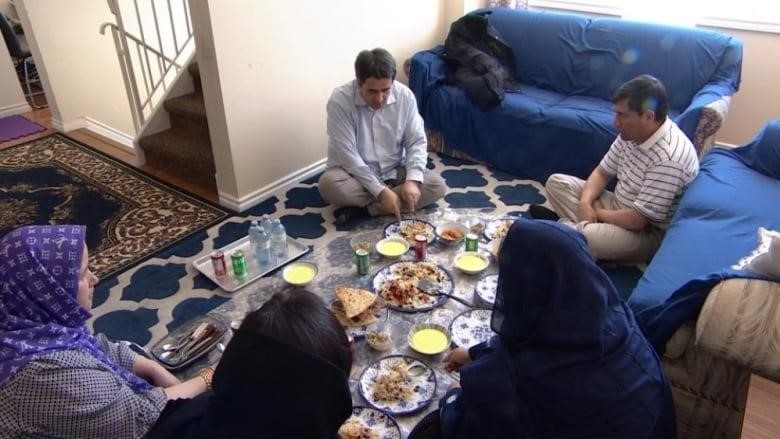 A family sits on carpeted floor to enjoy a meal together.