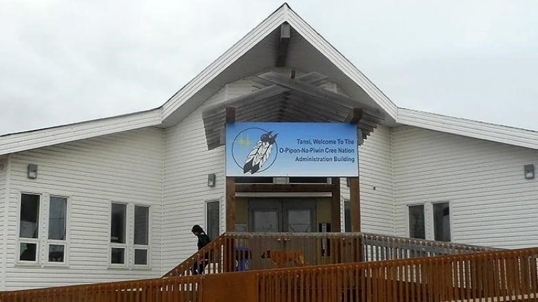 The O-Pipon-Na-Piwin Cree Nation band office is a white building with a pointed peak roof and a wooden wheelchair ramp in the front.