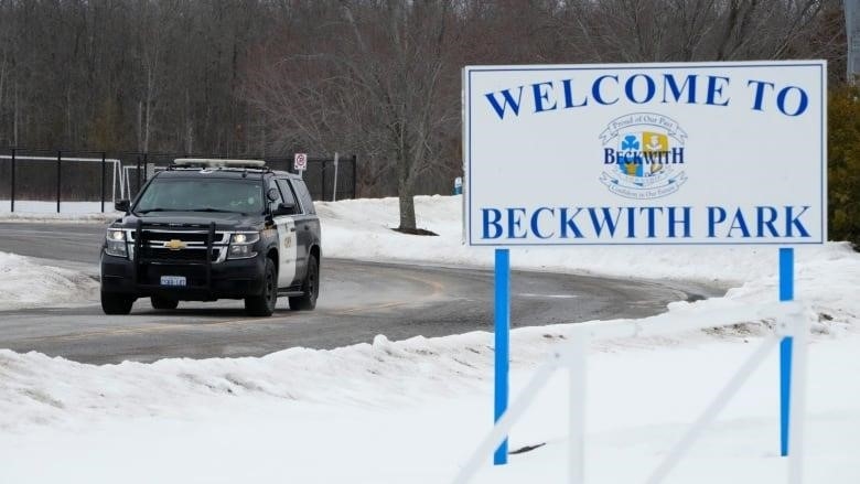 A police vehicle is parked on a road next to a sign saying 'Welcome to Beckwith Park.'