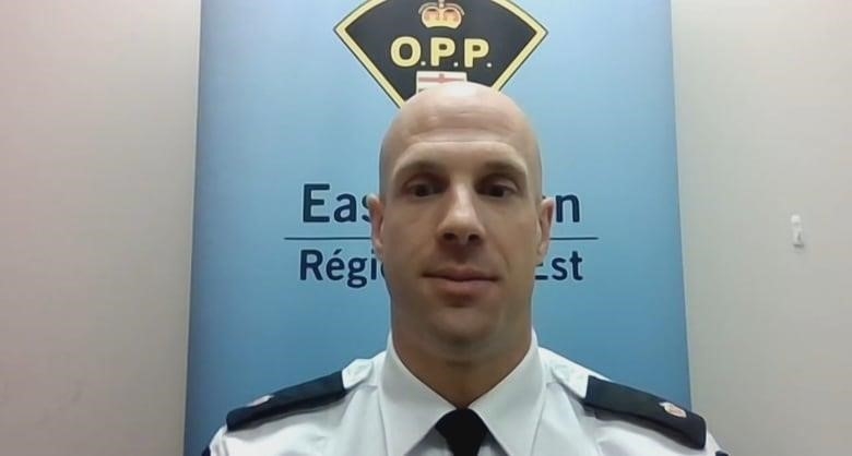 A man in a police uniform sits in front of the insignia for the Ontario Provincial Police.  