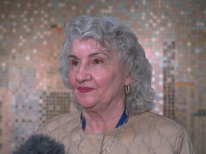 A woman stands in front of a microphone answering questions from a reporter.