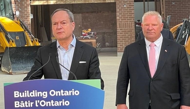 Photo of Finance Minister Peter Bethlenfalvy, left, stands behind a podium that reads 'Building Ontario," while Premier Doug Ford looks on.  