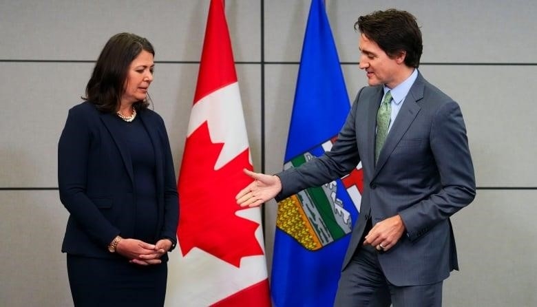 Alberta Premier Danielle Smith looks down at the hand of Prime Minister Justin Trudeau as he extends his hand for a handshake.