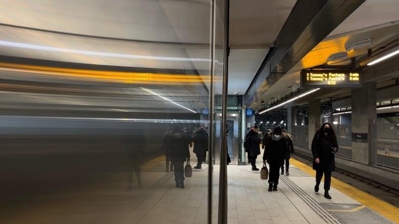 People walk along a train platform.