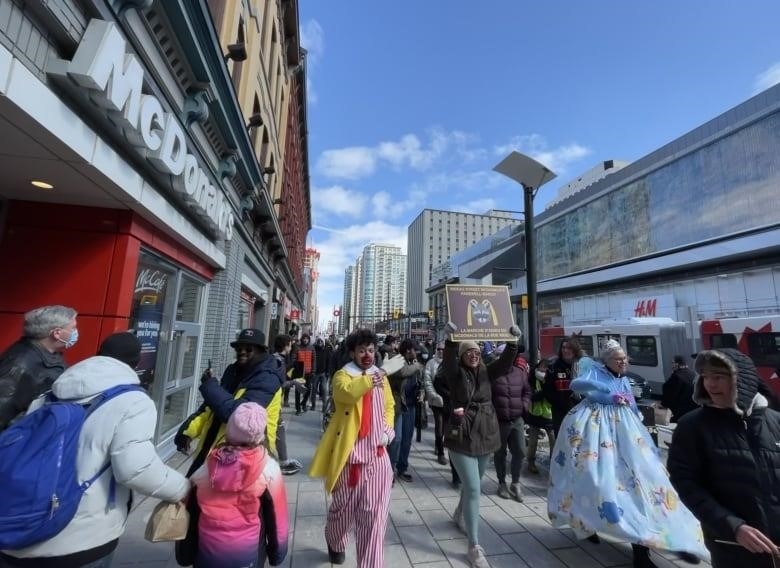 Marchers in costumes walk down a busy urban street.