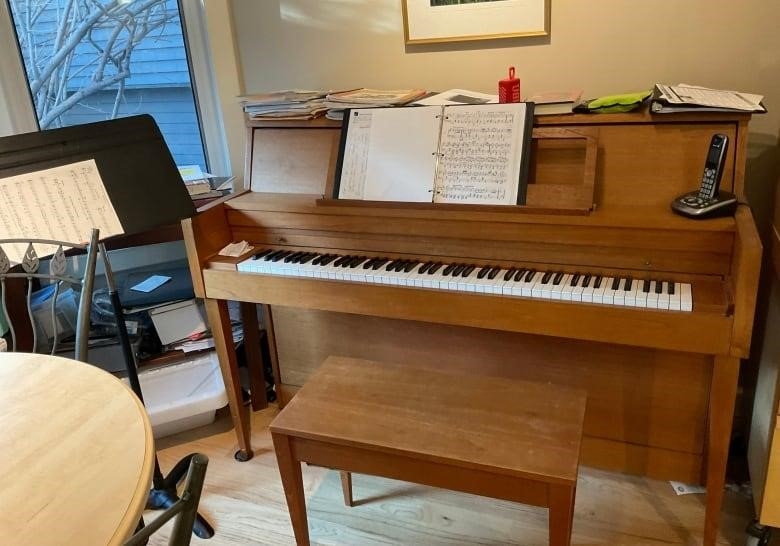 An upright piano with a pile of music books on top of it. 