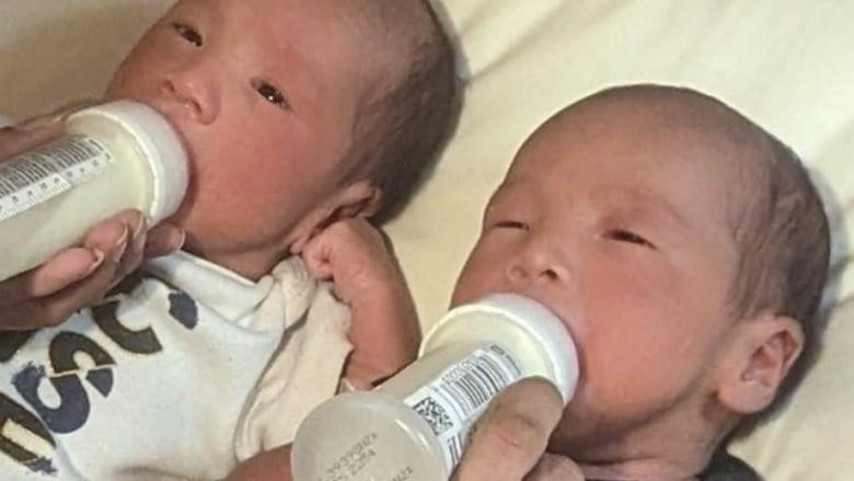 Twin babies with bottles, man's arm. 