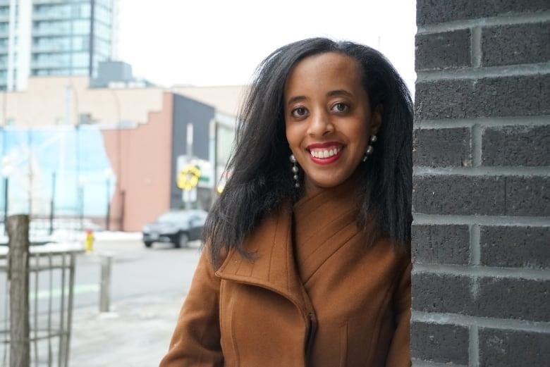 A woman standing outside leaning against a black brick wall.