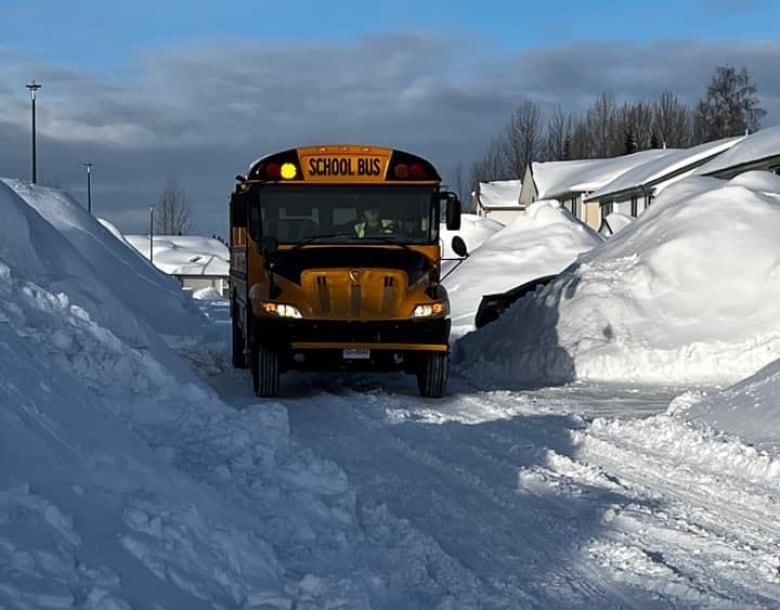 A school bus drives through snow piles taller than it.