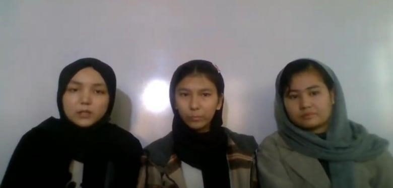 Three young girls sit in a row. They have head scarfs.