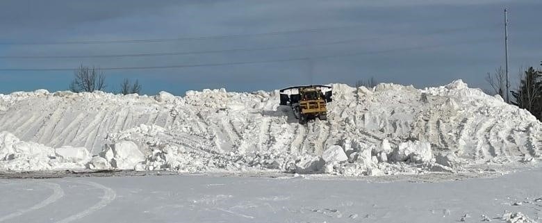 A piece of heavy machinery drives on a large pile of snow.