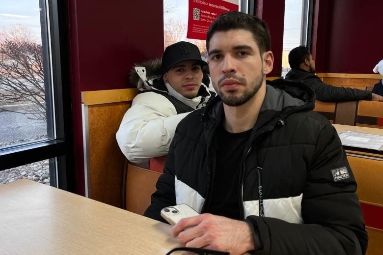 Steven, 24, and his 21-year-old friend, both from Venezuela, wait for the bus to New York City at the Mountain Mart bus stop and gas station Plattsburgh, NY on Tuesday.