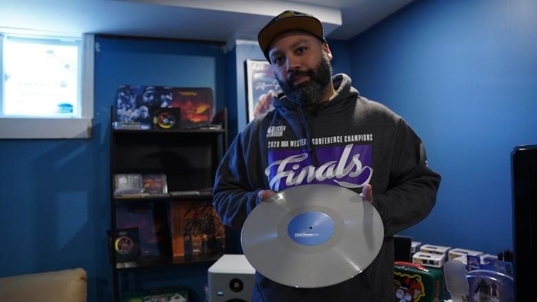 A man is shown holding a grey vinyl album and he is presenting it with both hands.