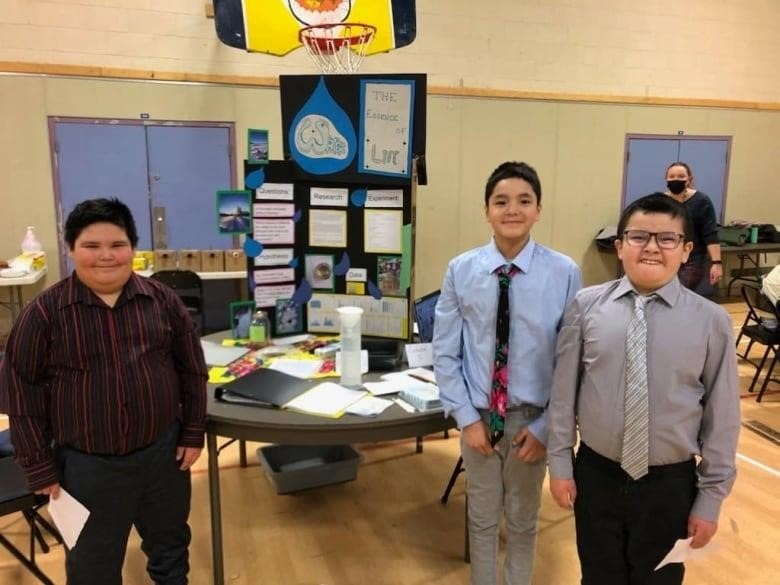 A group of three young Cree boys stands in front of their science project. 