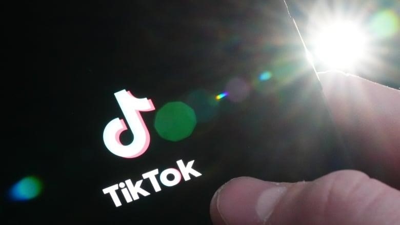 A person's holds an iPhone, showing the startup page of the TikTok app.