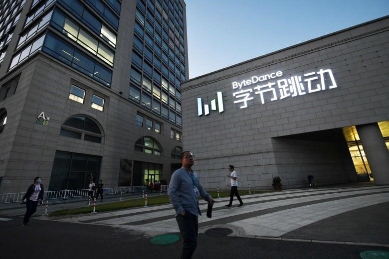 People walk past a grey brick building with lighted words in English and Chinese characters on the facade.