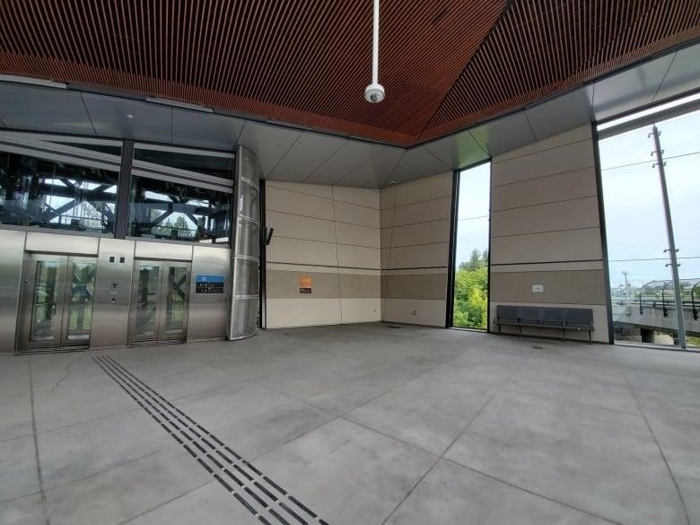 The inside of Tremblay station. Two grey elevators are on the left side of the photo, and a large open space is featured. A grey bench is on the photo's right side.