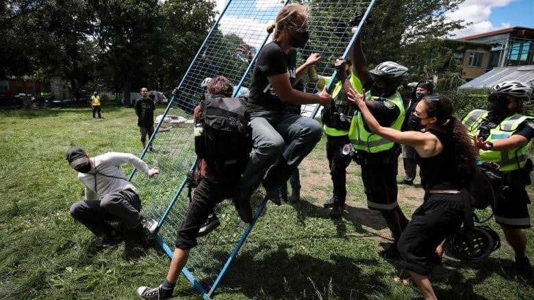 Supporters try to take down a fence as occupants of a homeless encampment at Toronto's Trinity Bellwoods Park await their possible eviction by police after workers enclosed the area with a fence on Tuesday.