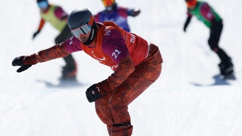 A para snowboarder wearing red travels down a snowy slope, with three competitors behind him.