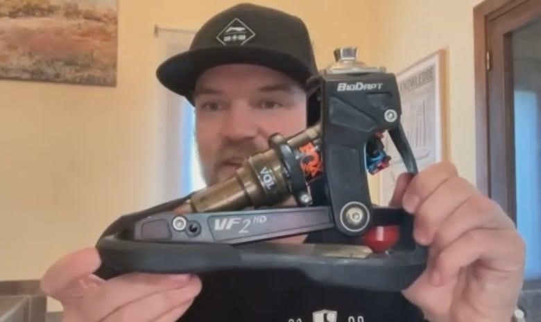 A man shows off a leg implement with a piston-like attachment while talking on a video chat.