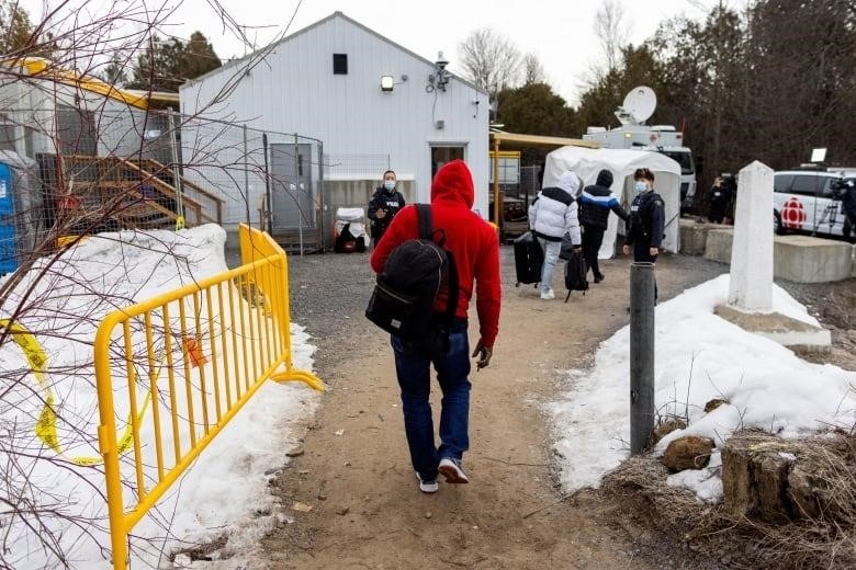 A Royal Canadian Mounted Police (RCMP) officer tells migrants to read the new border sign before they cross into Canada at Roxham Road, an unofficial crossing point from New York State to Quebec for asylum seekers, in Champlain, New York, U.S. March 25, 2023. 