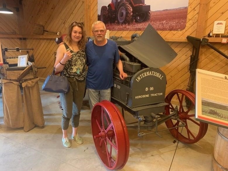 Father and daughter pose for a picture in front of an antique car while on vacation. 