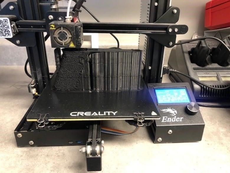 A photo shows a 3D printer sitting on a table in a brightly lit room.