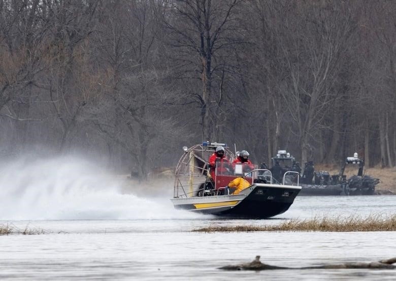 People on two boats search a marshy area.