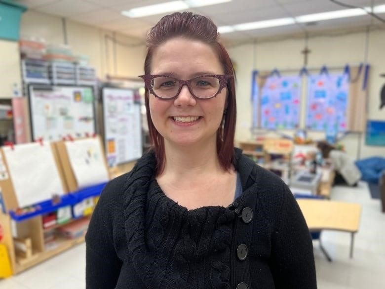 A woman in black sweater and purple glasses smiles.