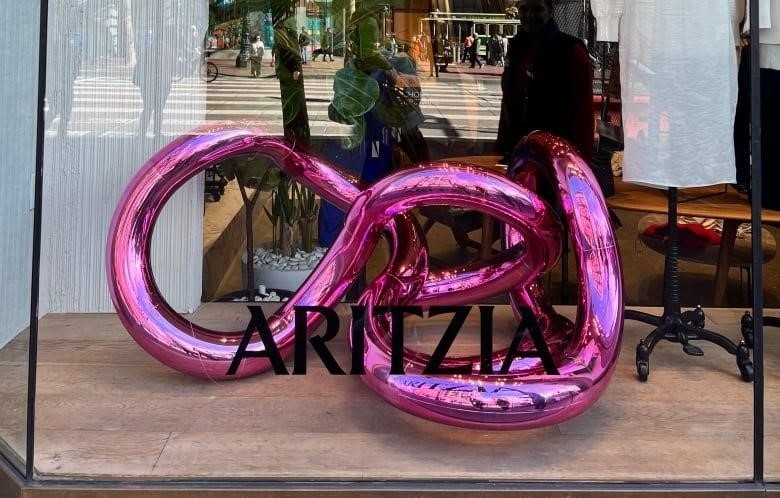 A pink, curved sculpture is pictured inside a window display for a store inside a mall. 