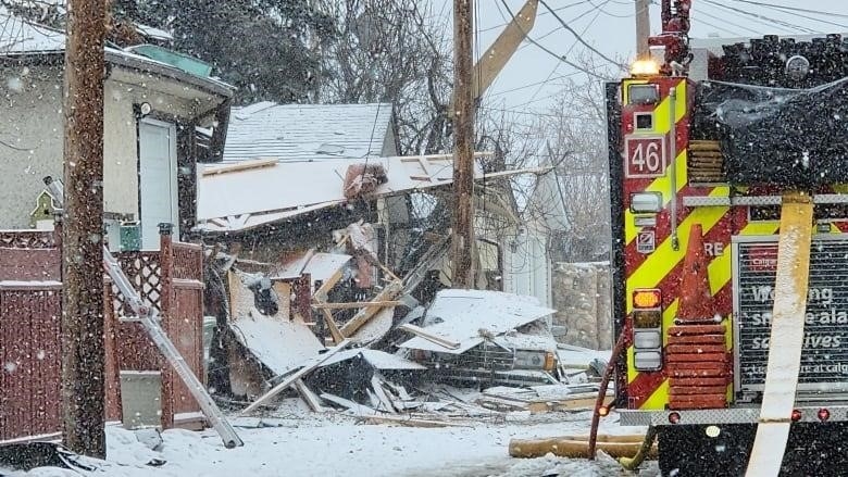 A pile of debris sits where a home once stood as spring snow falls on a fire engine. 