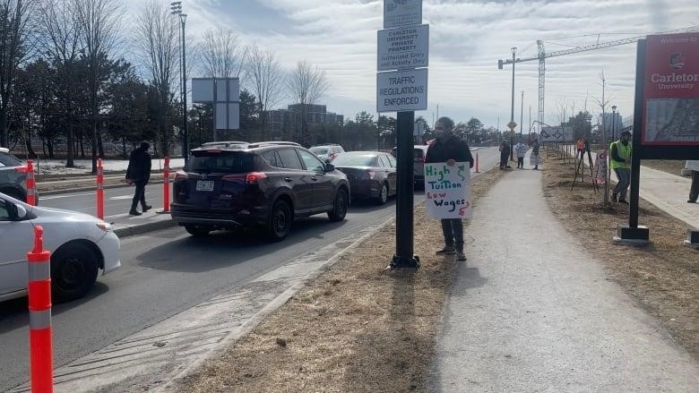 Workers on a picket line hold up a line of cars going onto a university campus.