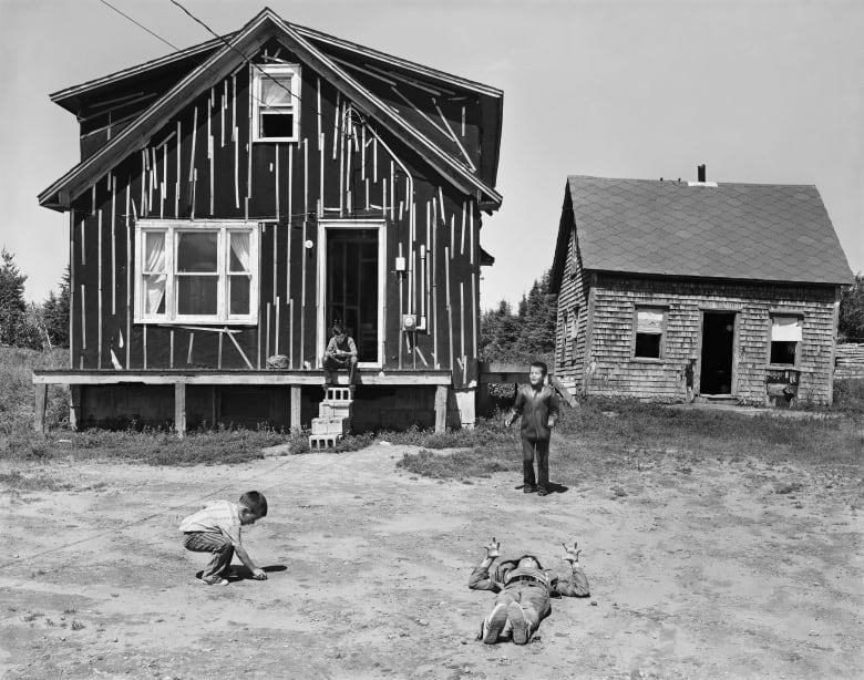 black and white photo of young children playing outside unfinished homes in dirt
