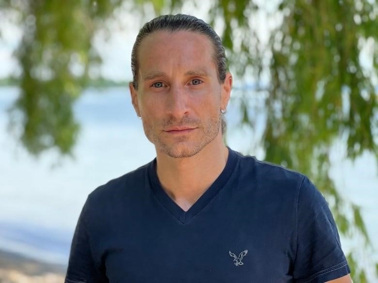 A man stands in front of a lake looking at the camera.