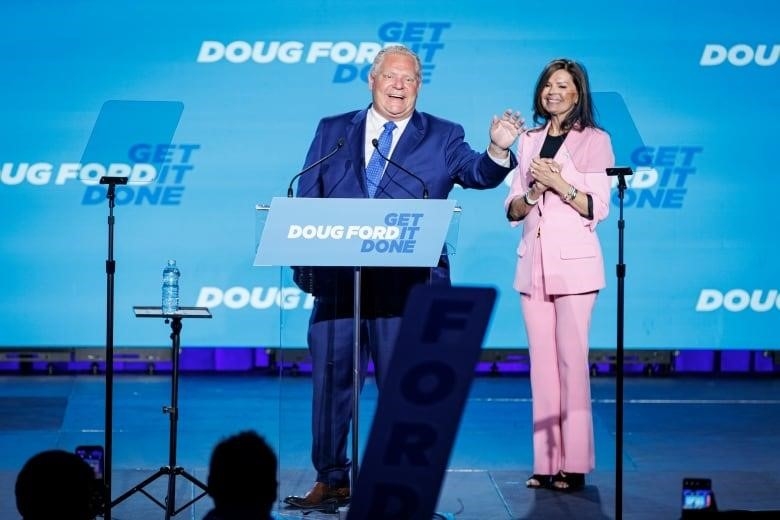 Doug Ford waves on stage while his wife is standing beside him.  