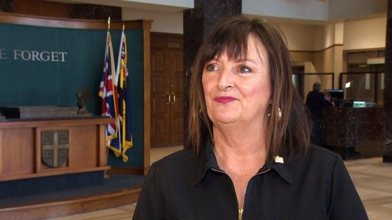 A woman with short brown hair wearing a black top. She's standing in the lobby of a government building.