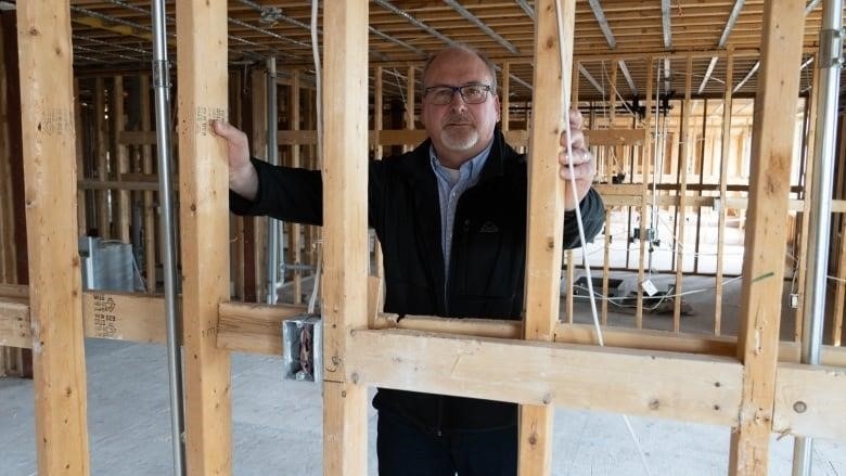 A man stands in front of wall studs with exposed electrical wiring.