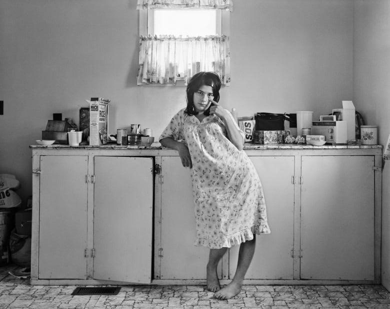black and white photo of young woman in night gown standing in 1970s kitchen